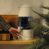 Aqualine waterfilter op houten aanrecht met plant ervoor en arm met hand die water tapt